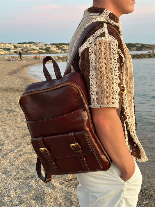 Homme portant un sac à dos en cuir marron au bord de l'eau, style décontracté en été.
