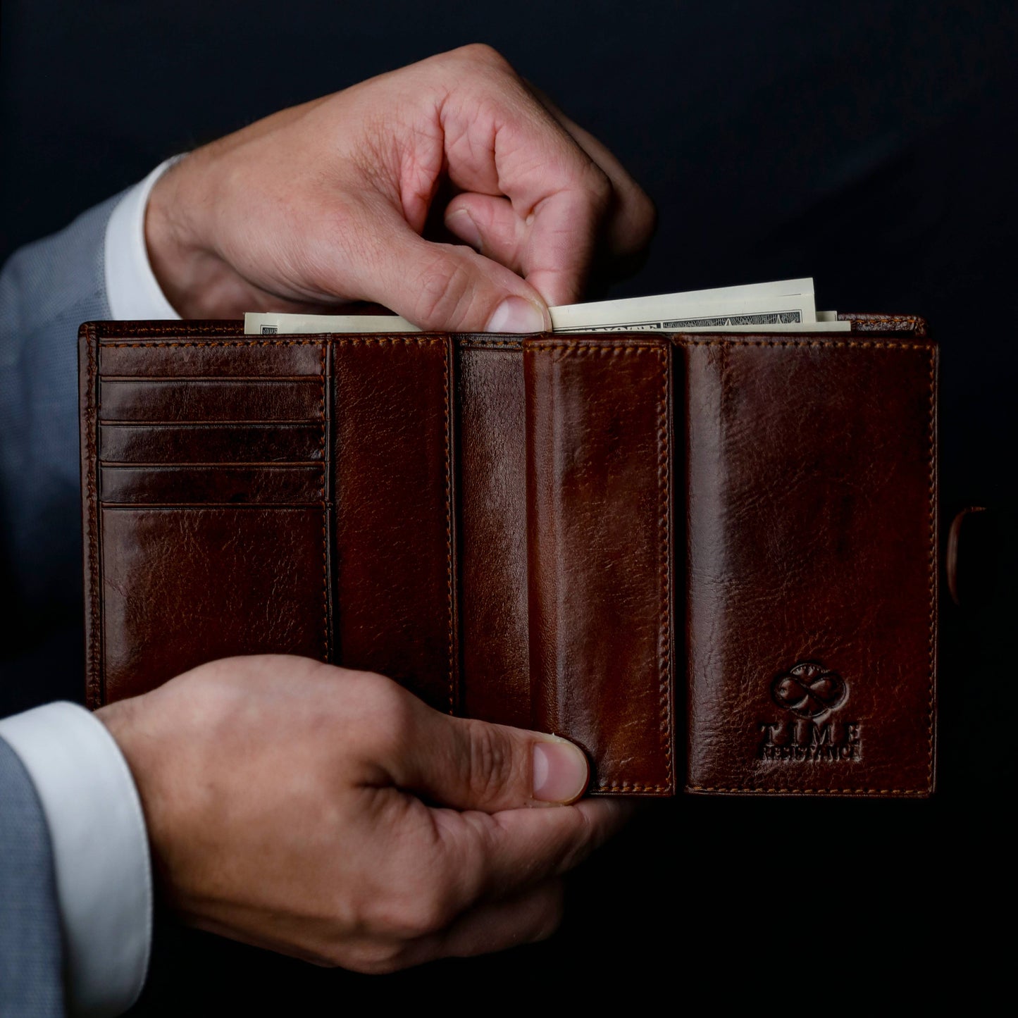 Brown leather wallet with money held by a person against a dark background