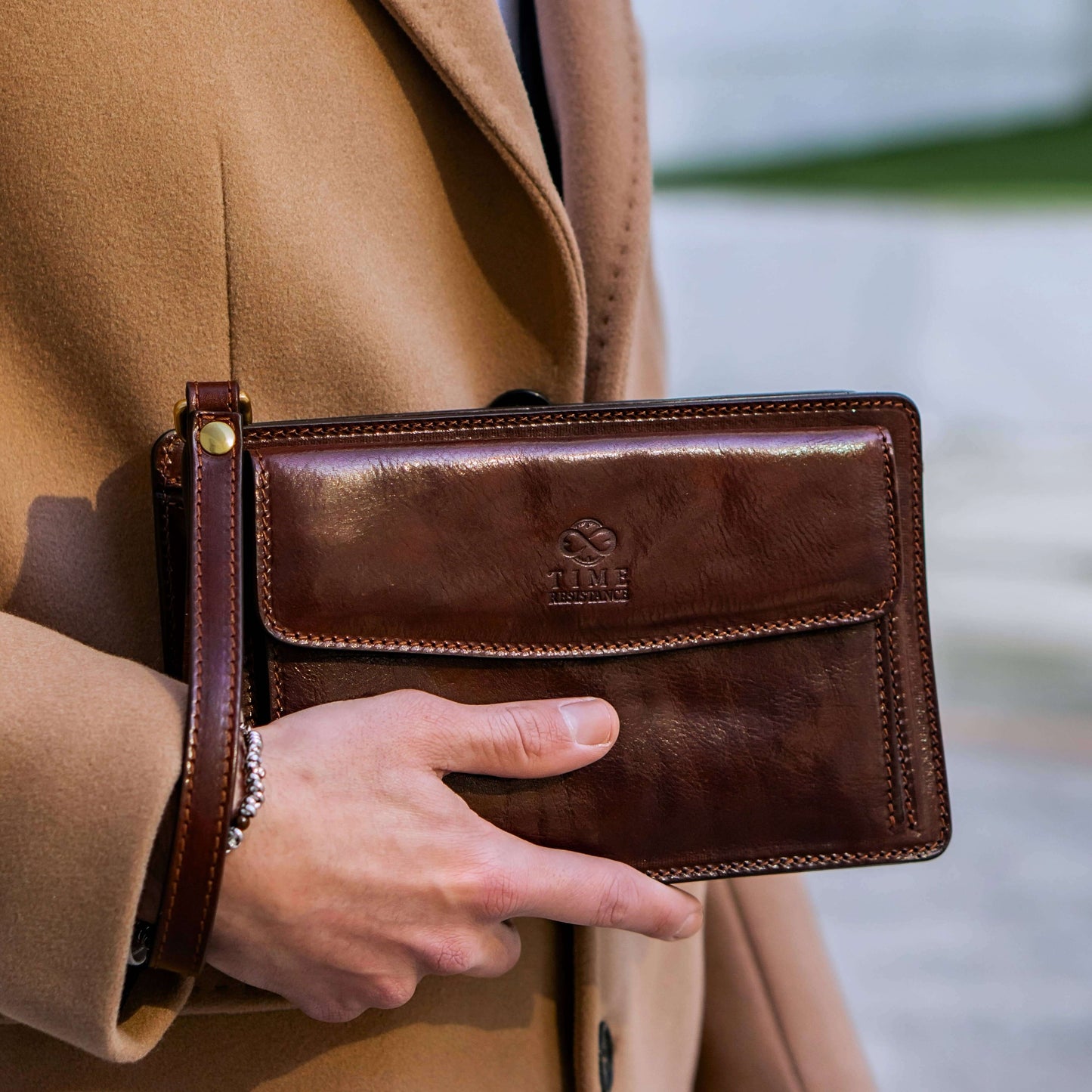 Brown leather wallet held by a person wearing a tan coat, with a blurred background.