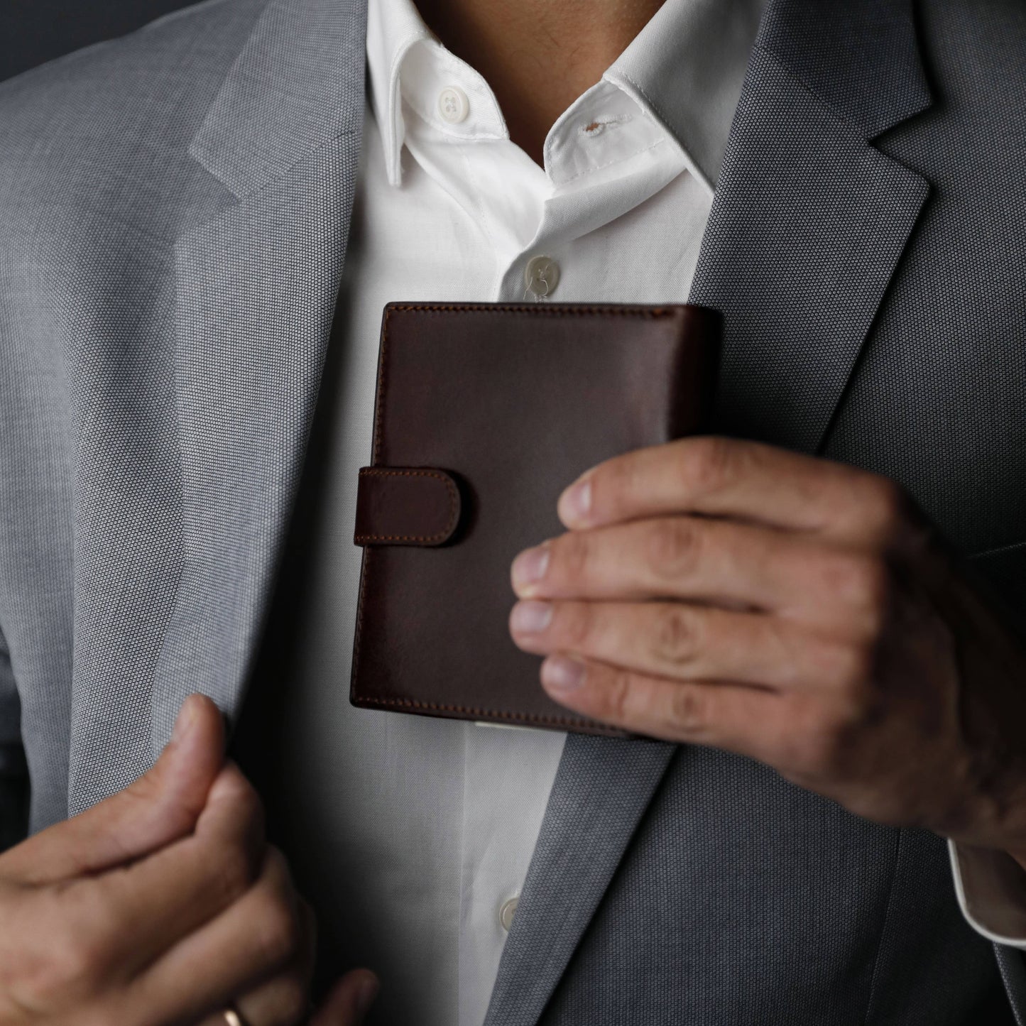 Person holding a brown leather wallet with a gray suit jacket and white shirt