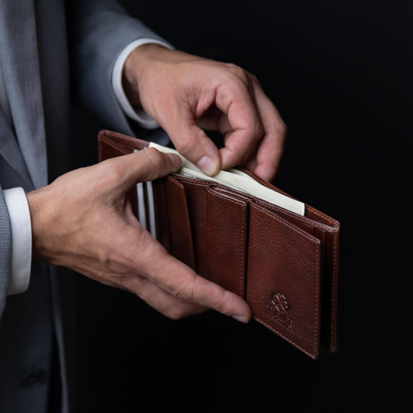 Brown leather wallet being held by a person in a suit against a dark background