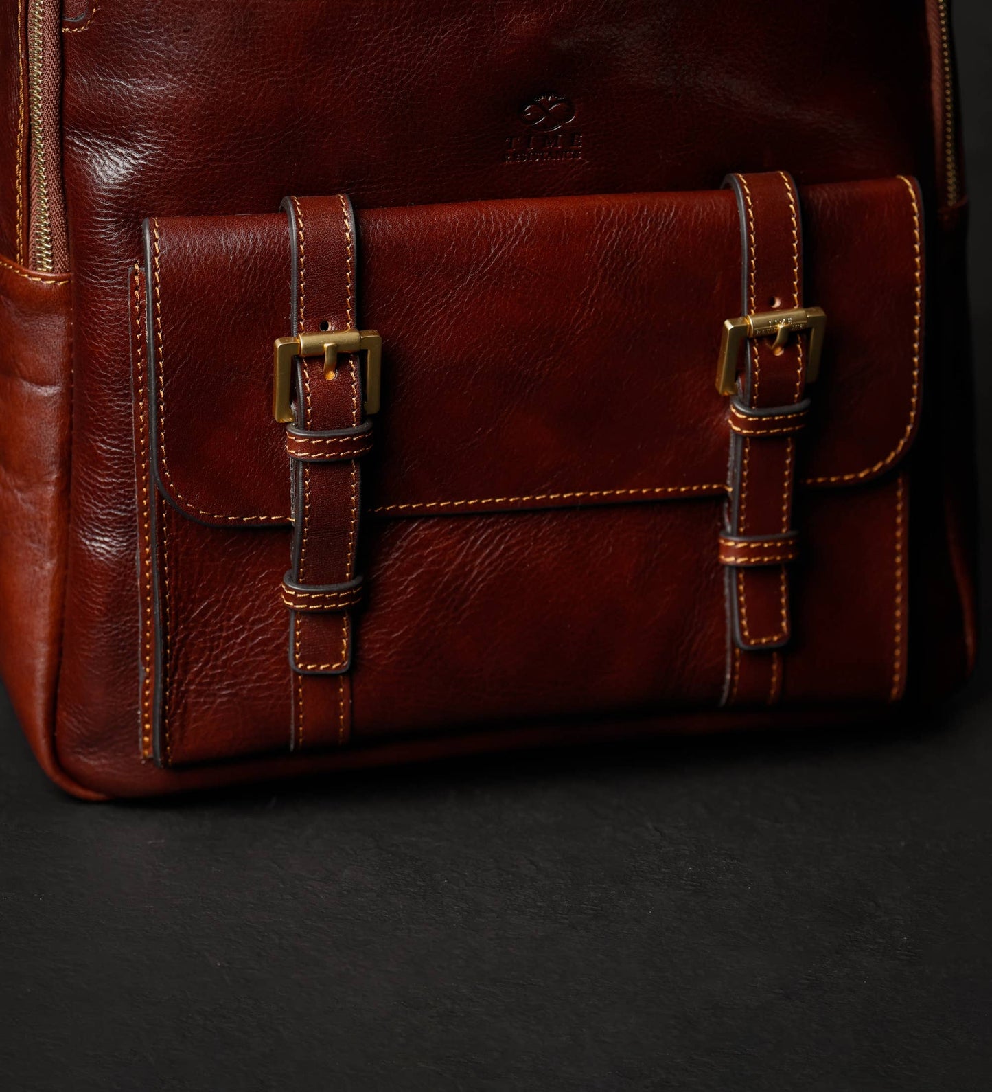 Close-up of a brown leather bag with gold buckles on a black background