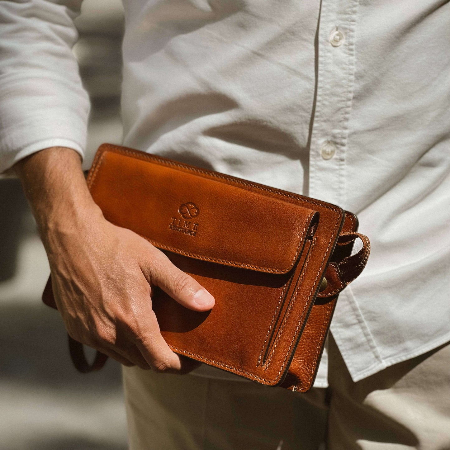 Person holding a brown leather wallet with a visible brand logo.