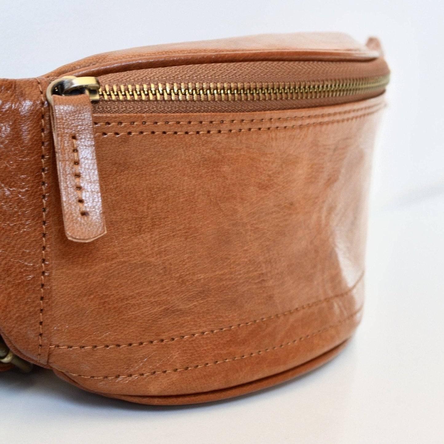 Brown leather waist bag with gold zipper on a light gray background