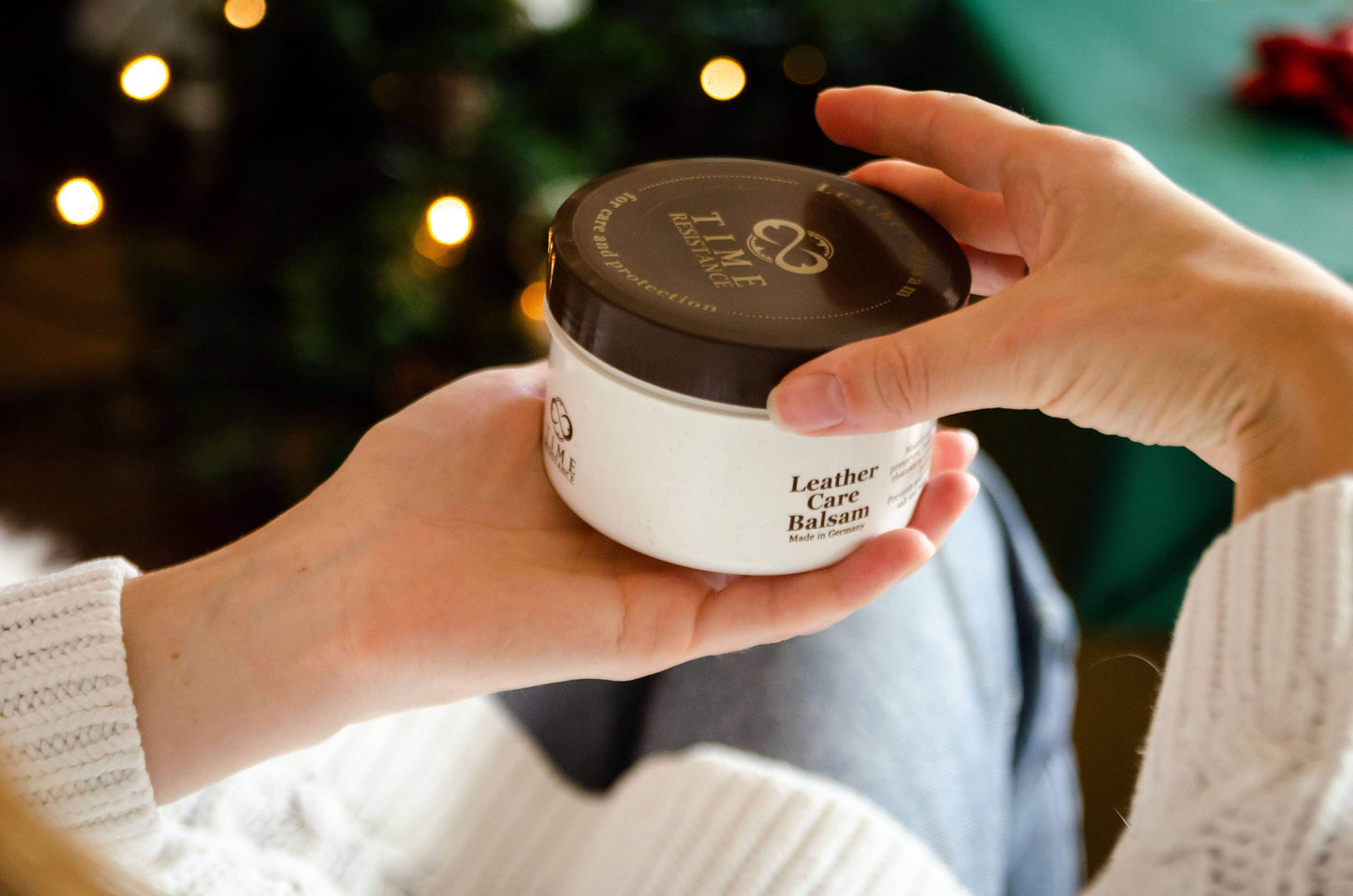 Person holding a jar of Leather Care Balm, perfect for nourishing and protecting leather items.