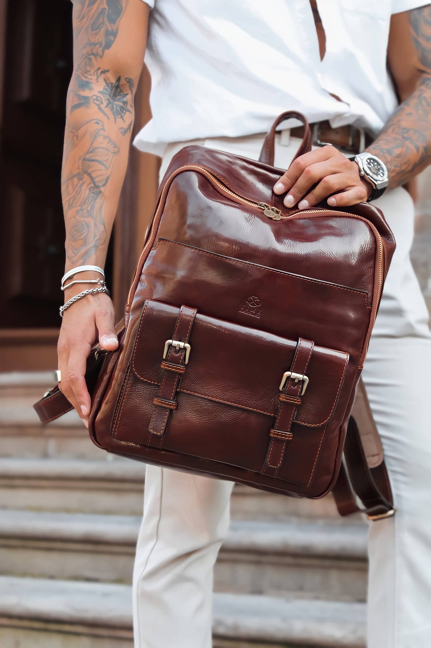 Person holding a brown leather backpack outdoors