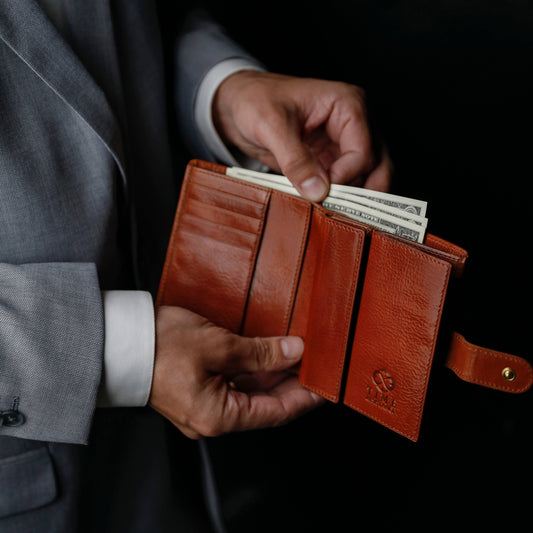 Person holding a brown leather wallet with money against a dark background
