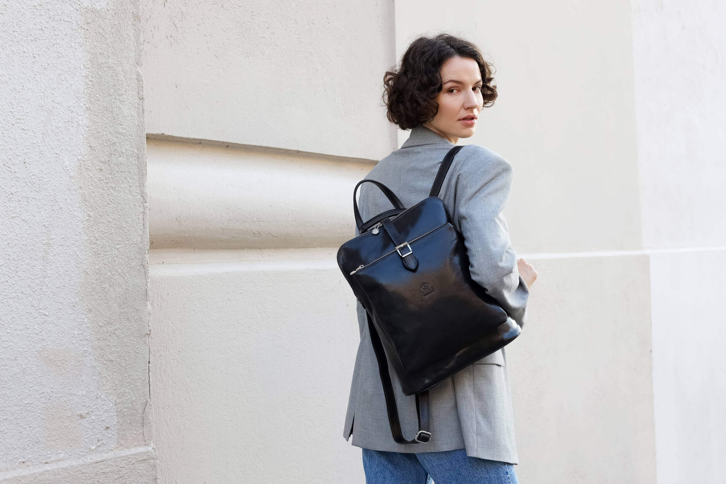 Woman holding a black backpack against a light-colored wall