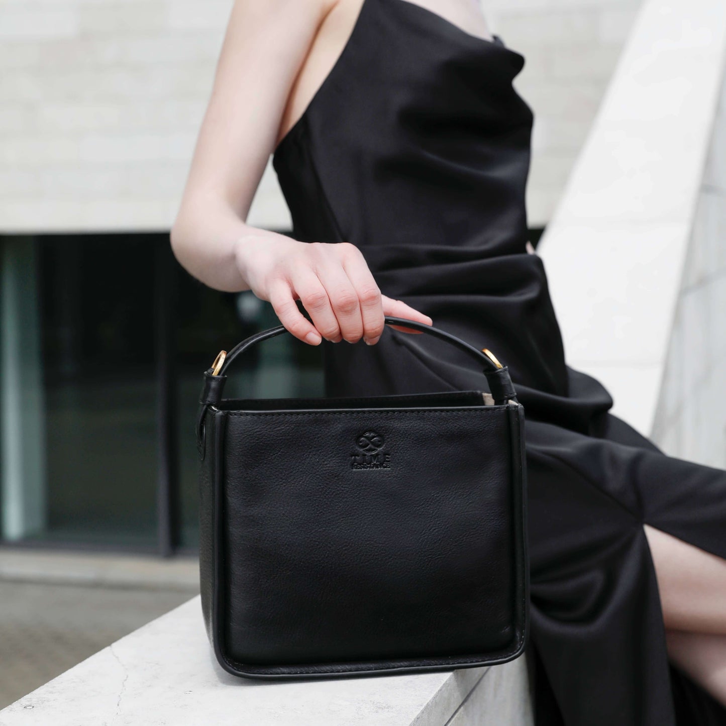 Elegant woman holding a black leather handbag, showcasing its versatility and refined design.
