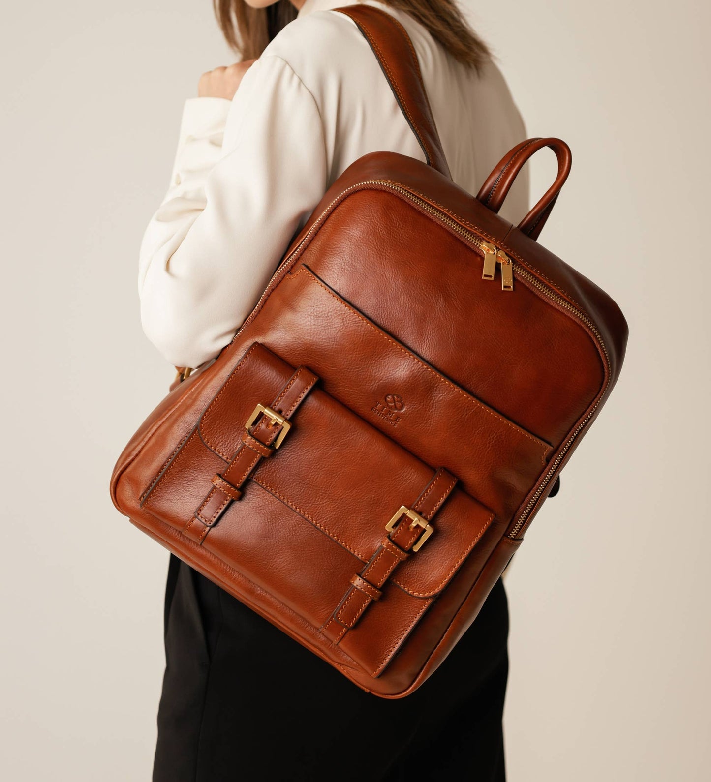 Brown leather backpack worn by a person on a beige background