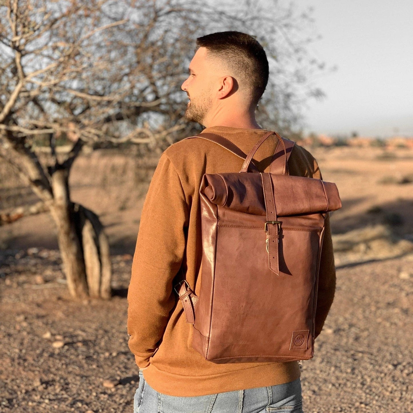 Man wearing a brown leather backpack in a desert setting