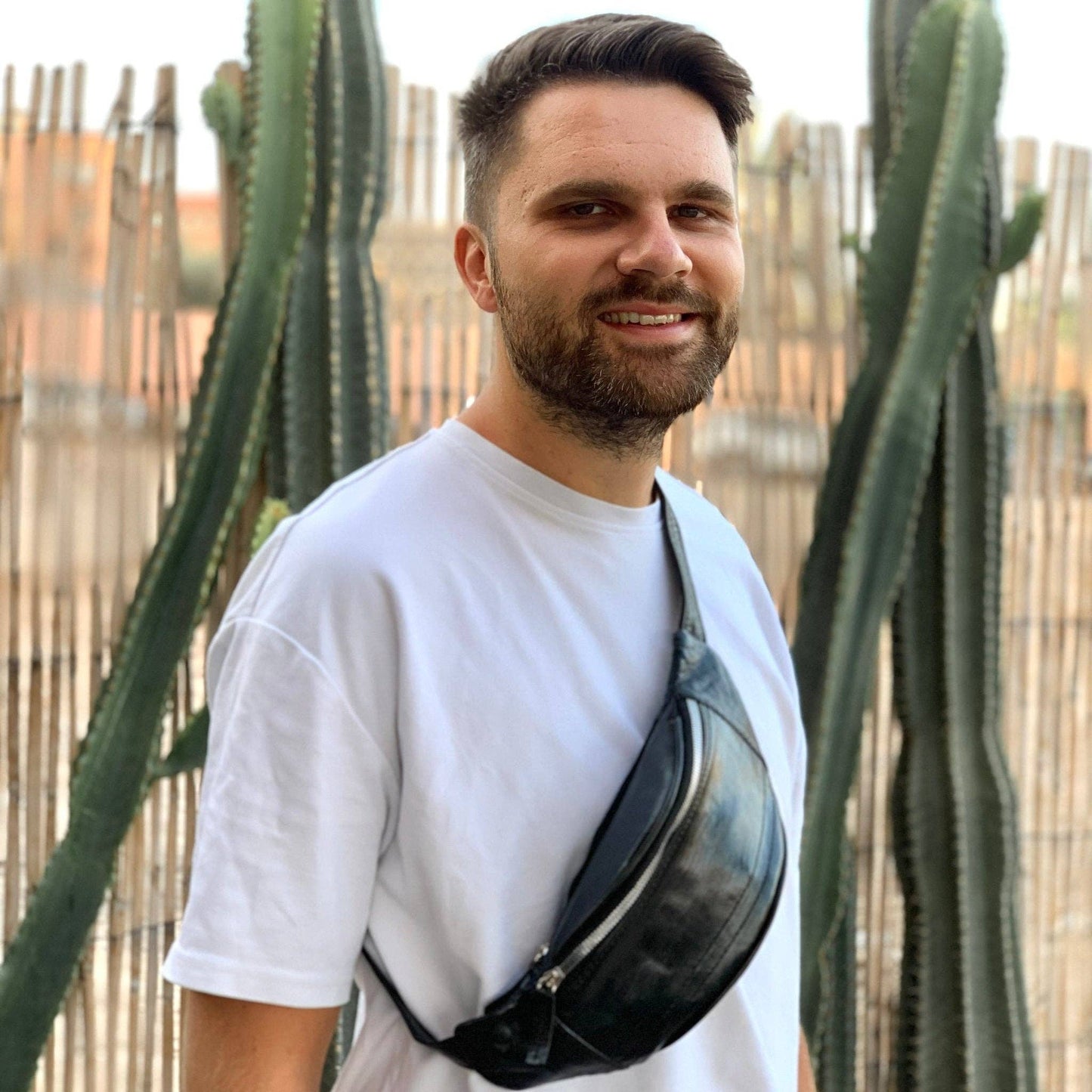 Man wearing a black fanny pack in front of cacti