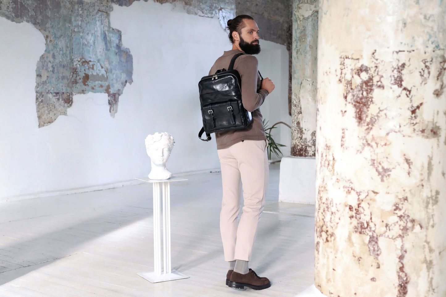 Man with a beard wearing a black backpack in an art gallery setting.
