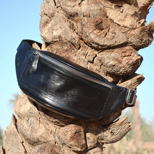 Black leather waist bag on a wooden surface with a natural background