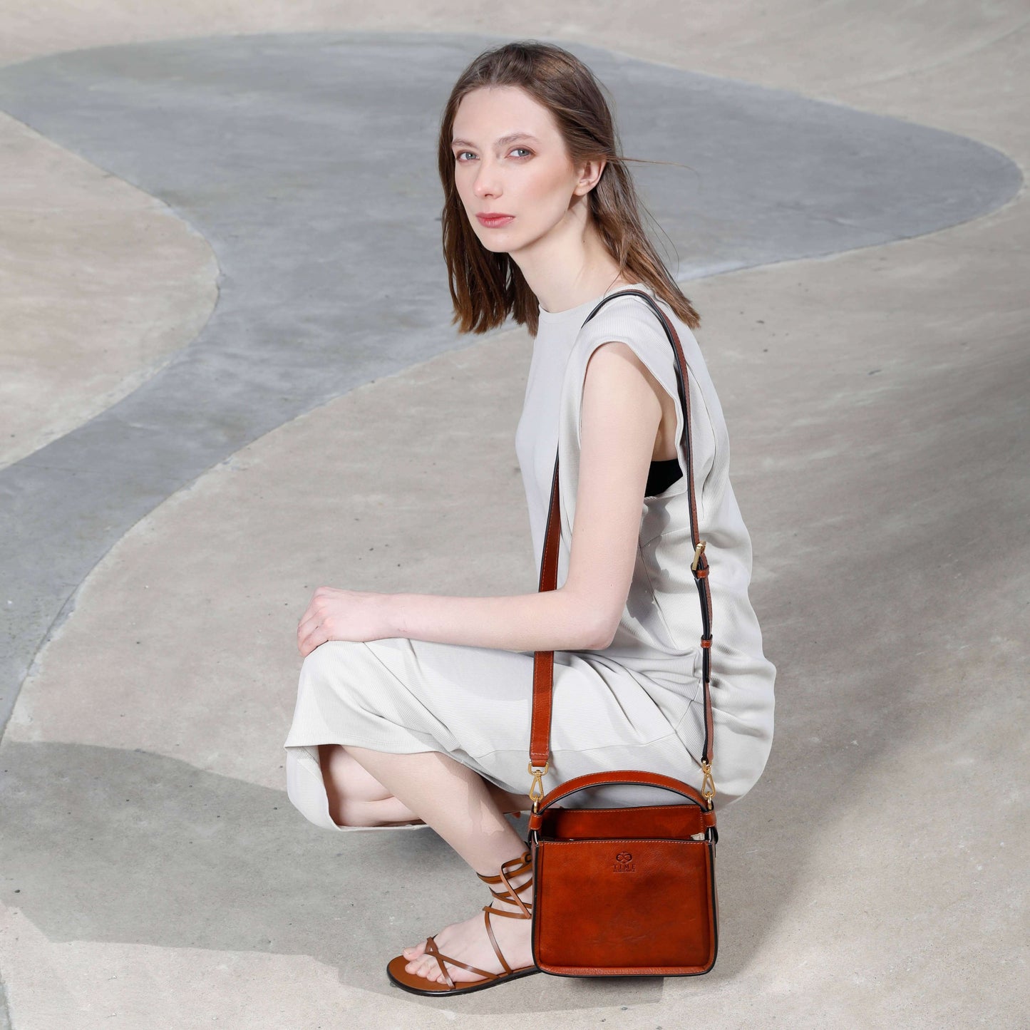 Woman in a stylish outfit featuring the Alms for Oblivion leather handbag in brown, showcasing versatility and elegance.