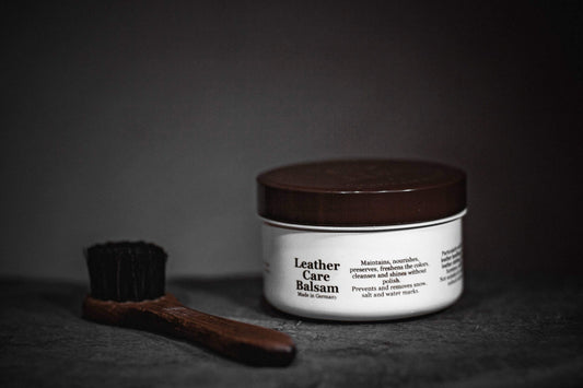 Leather Care Balm jar next to a brush, ideal for nourishing and protecting leather items.
