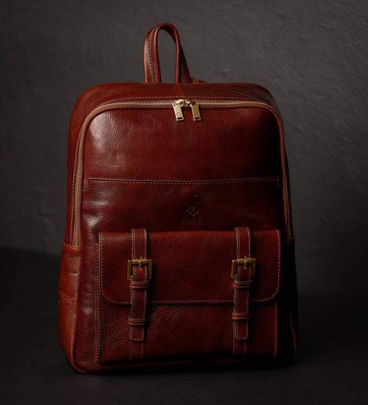Brown leather backpack with gold zippers on a dark background