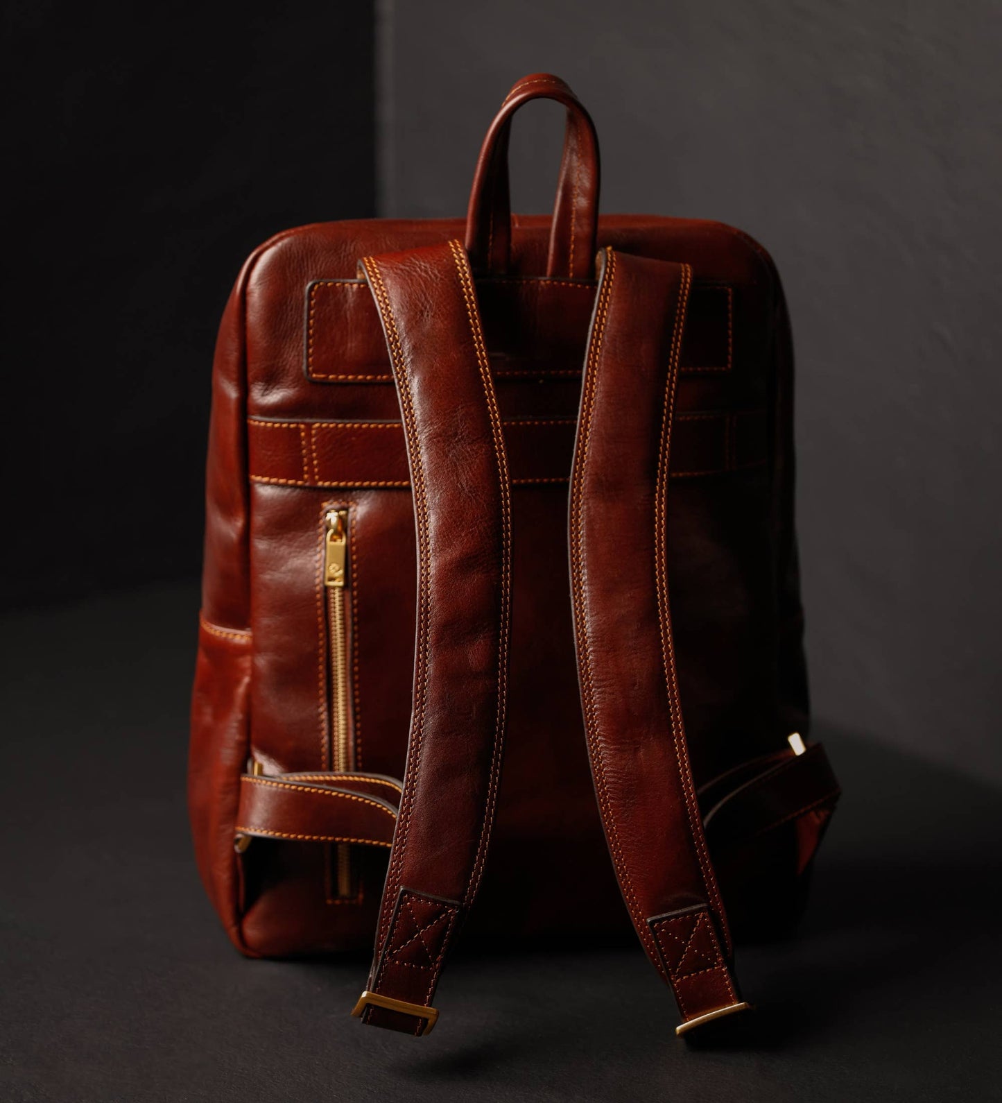 Brown leather backpack with gold zipper on a dark background