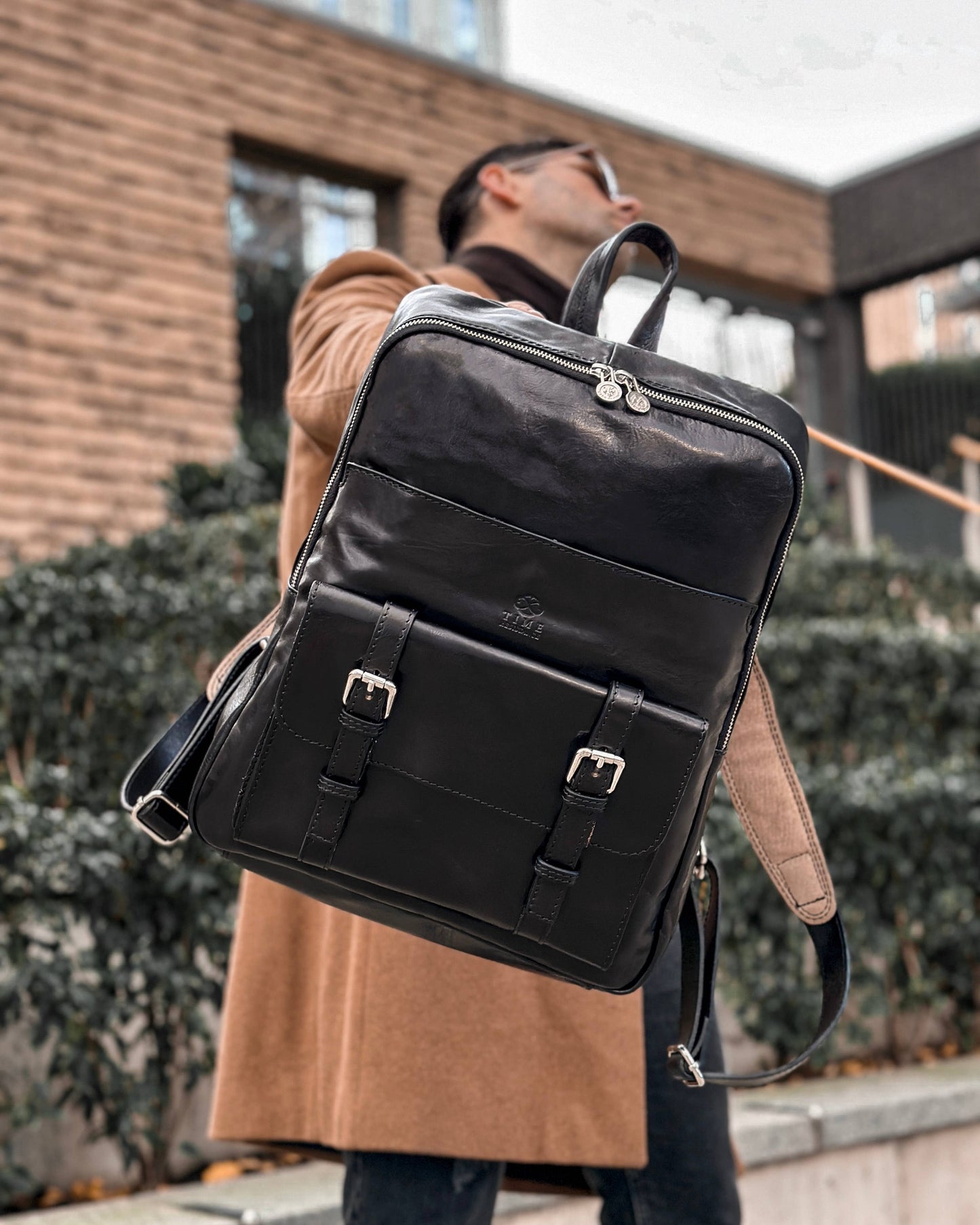 Person wearing a black backpack outdoors with a brick building in the background