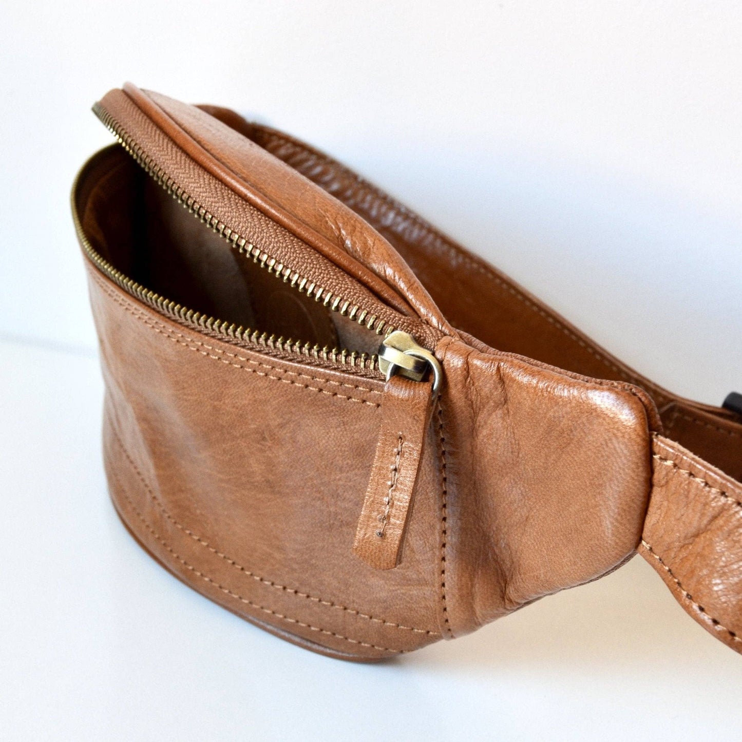 Brown leather waist bag with a gold zipper on a white background