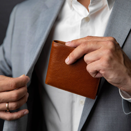 Person holding a brown leather wallet with a gray suit jacket and white shirt