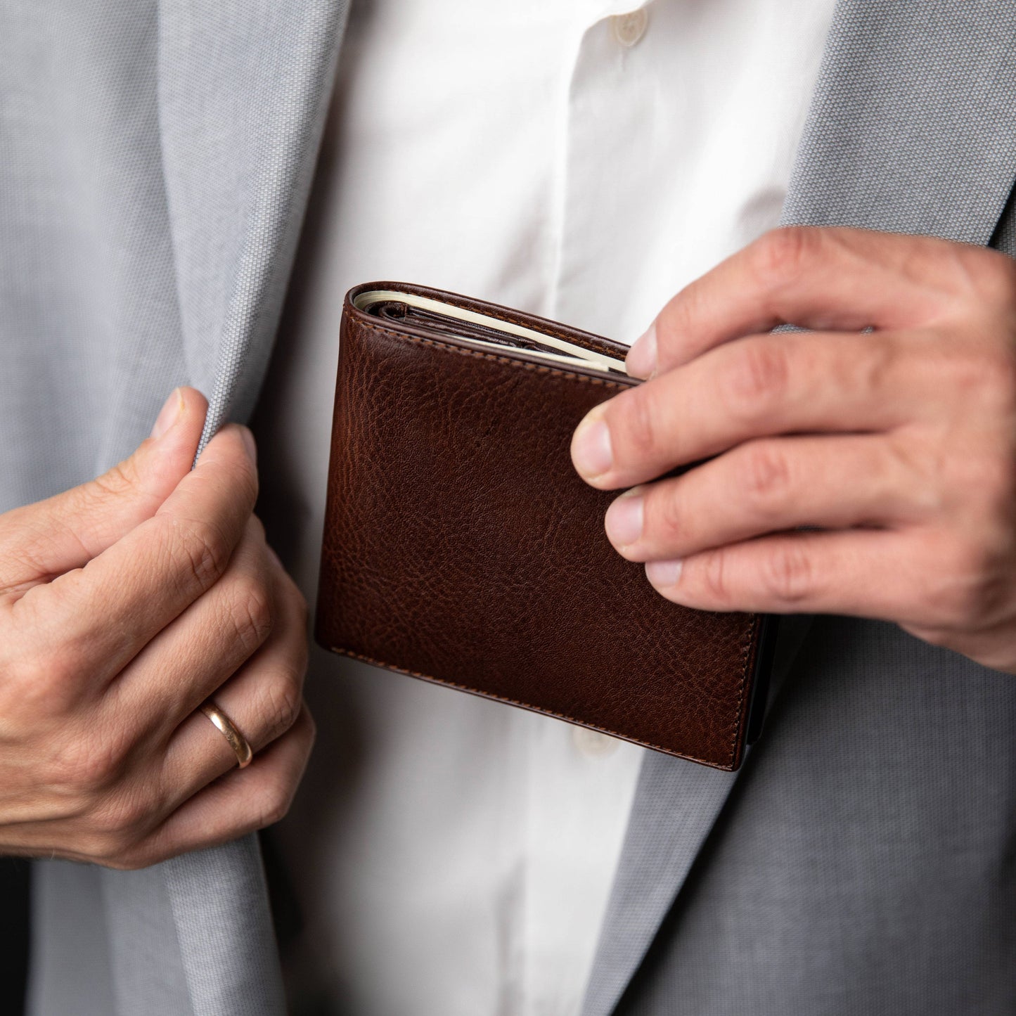 Brown leather wallet held by a person wearing a gray suit and white shirt.