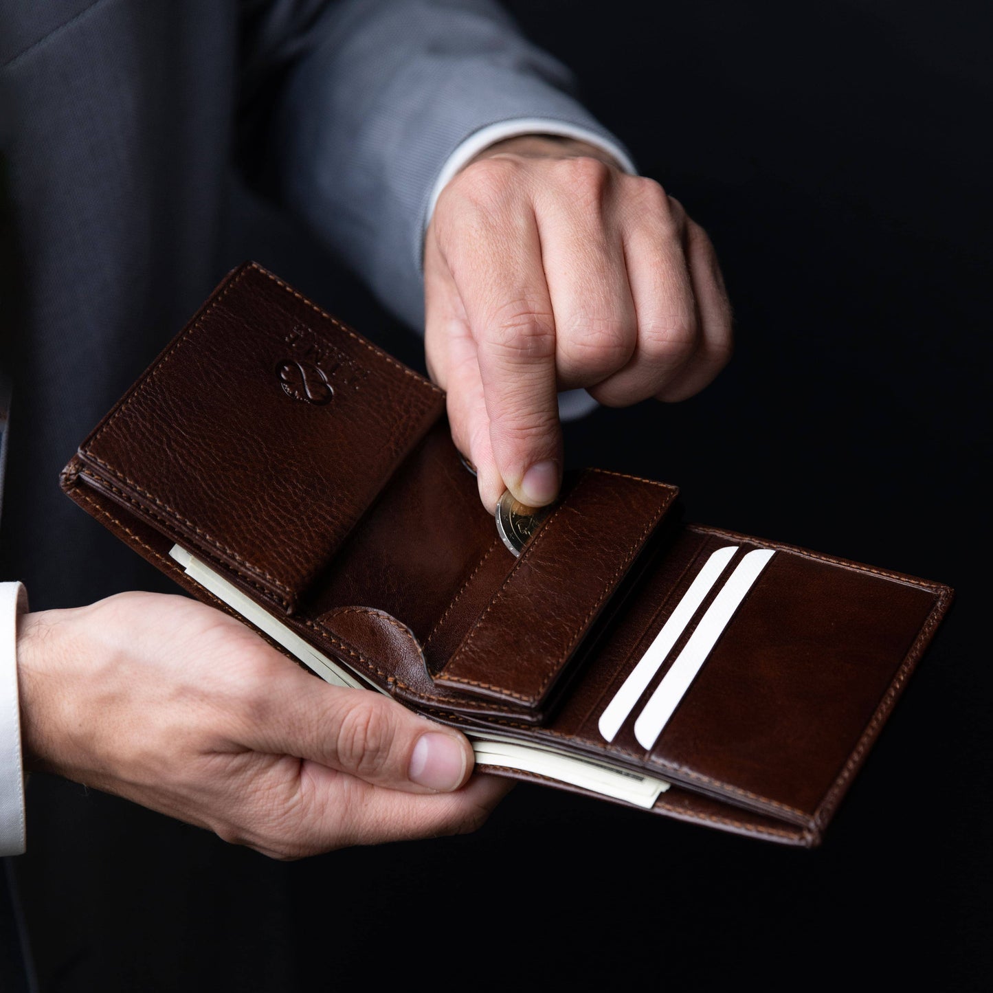 Brown leather wallet with card slots held by a person against a dark background