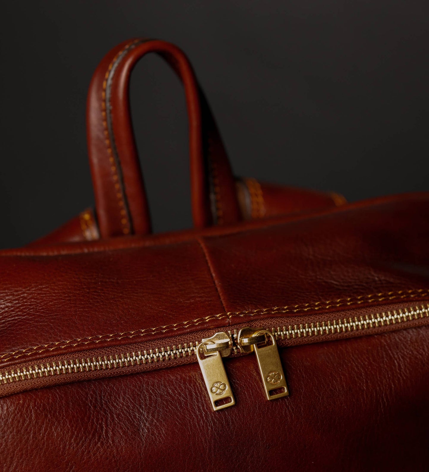 Close-up of a brown leather bag with a gold zipper on a dark background