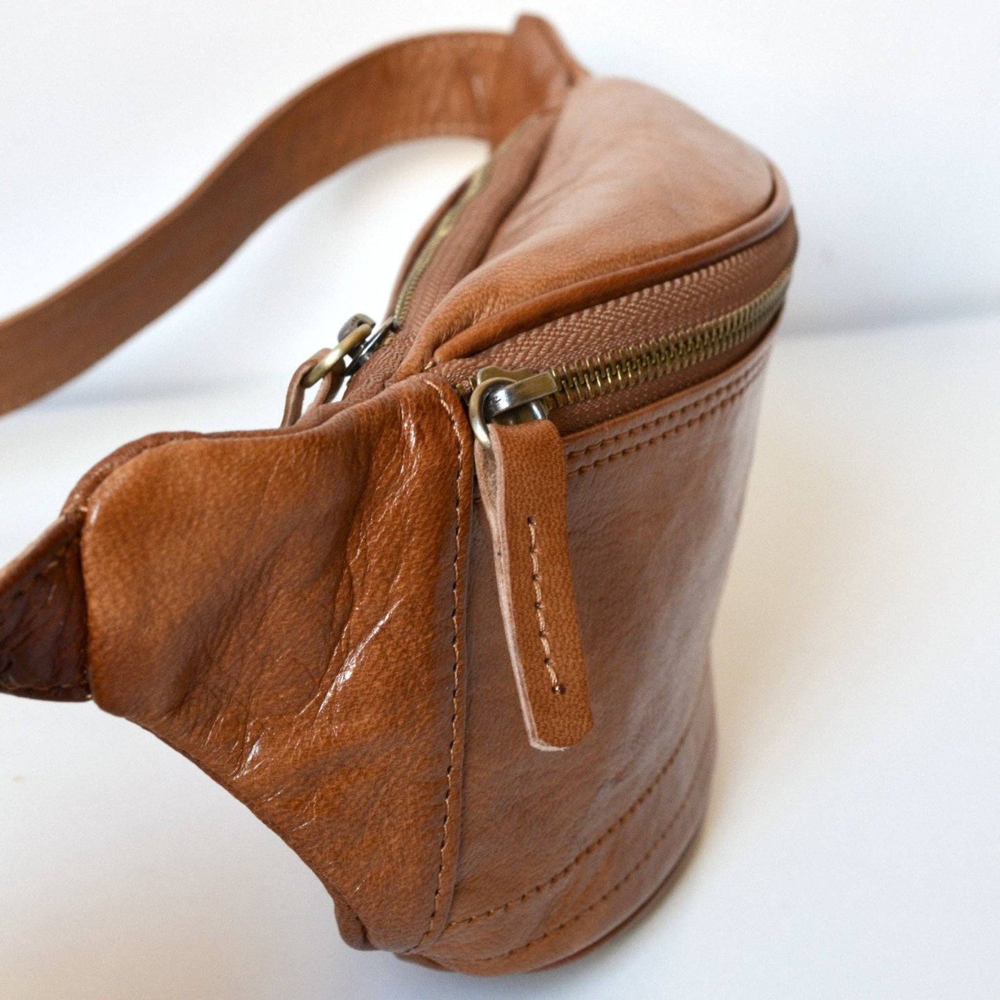 Brown leather waist bag with gold zipper on a white background
