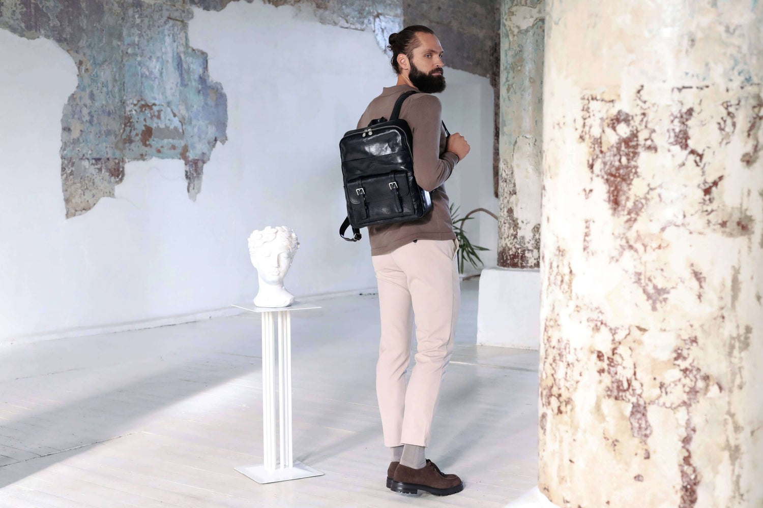 Man wearing a premium leather backpack in a stylish, minimalist interior setting.