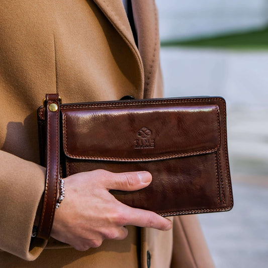 Brown leather wallet held by a person wearing a tan coat, with a blurred background.