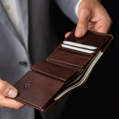Brown leather wallet held by a person in a suit against a dark background