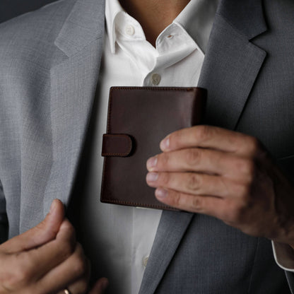 Person holding a brown leather wallet with a gray suit jacket and white shirt