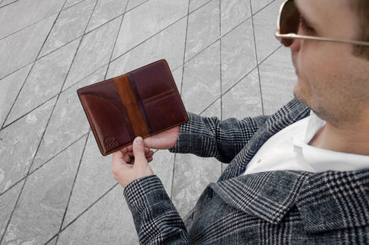 Man holding a brown leather wallet on a tiled pavement