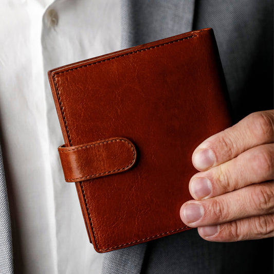 Brown leather wallet held by a person wearing a gray suit.
