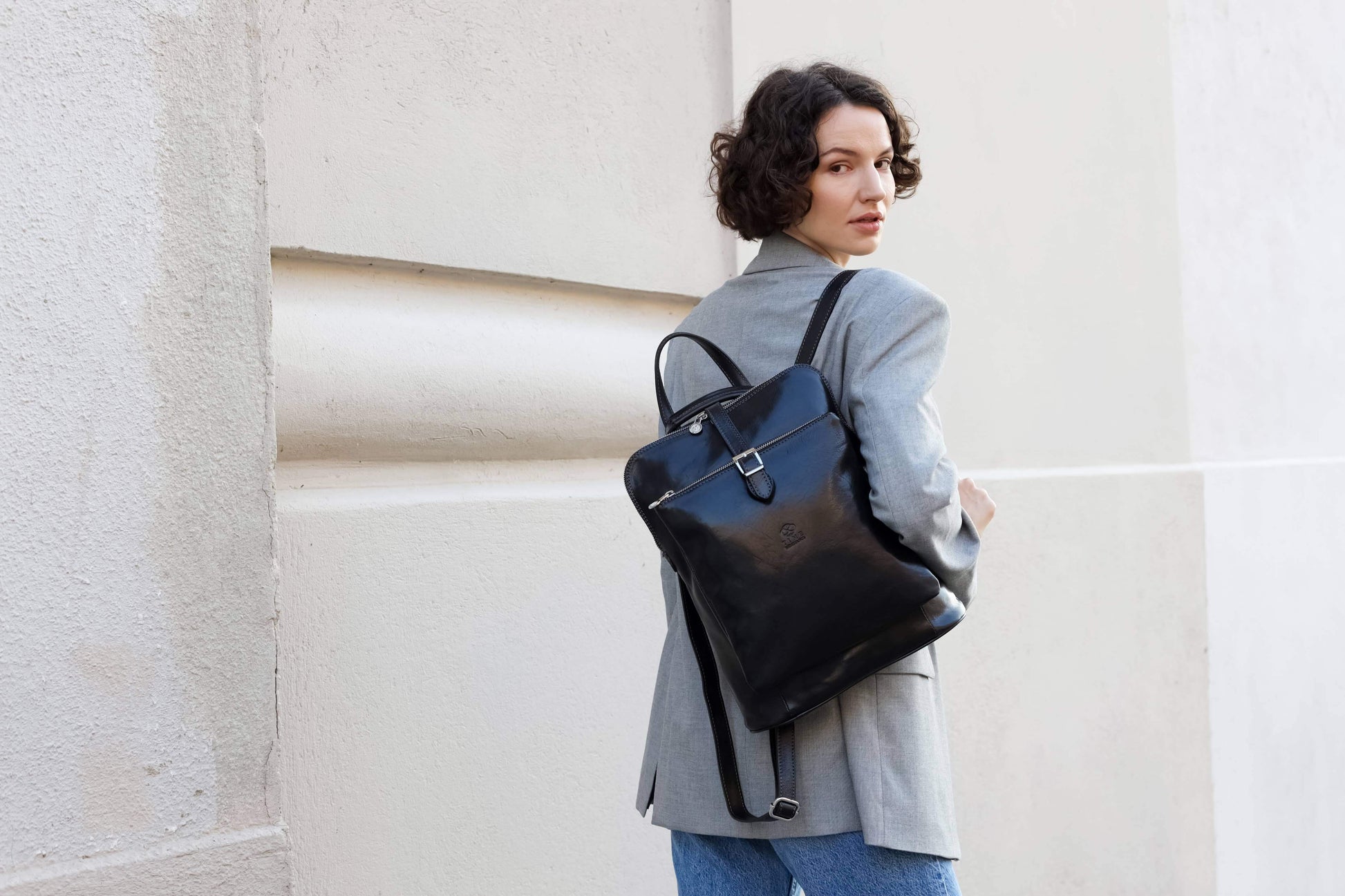 Woman holding a black backpack against a light-colored wall