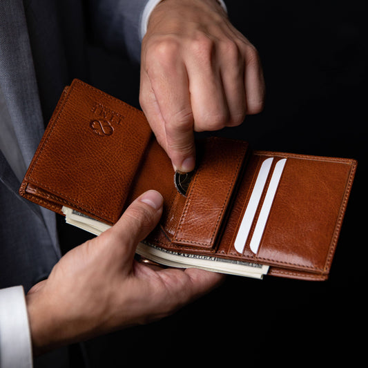 Brown leather wallet with money being inserted, held by a person in a suit.