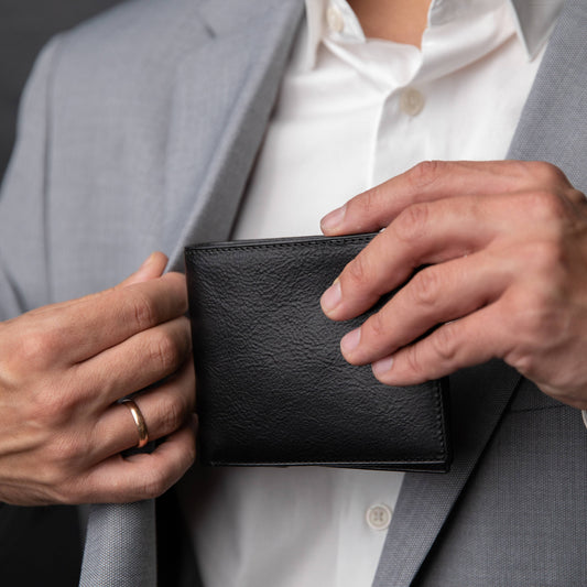 Person holding a black leather wallet with a gray suit and white shirt