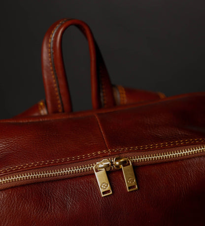 Close-up of a brown leather bag with a gold zipper on a dark background